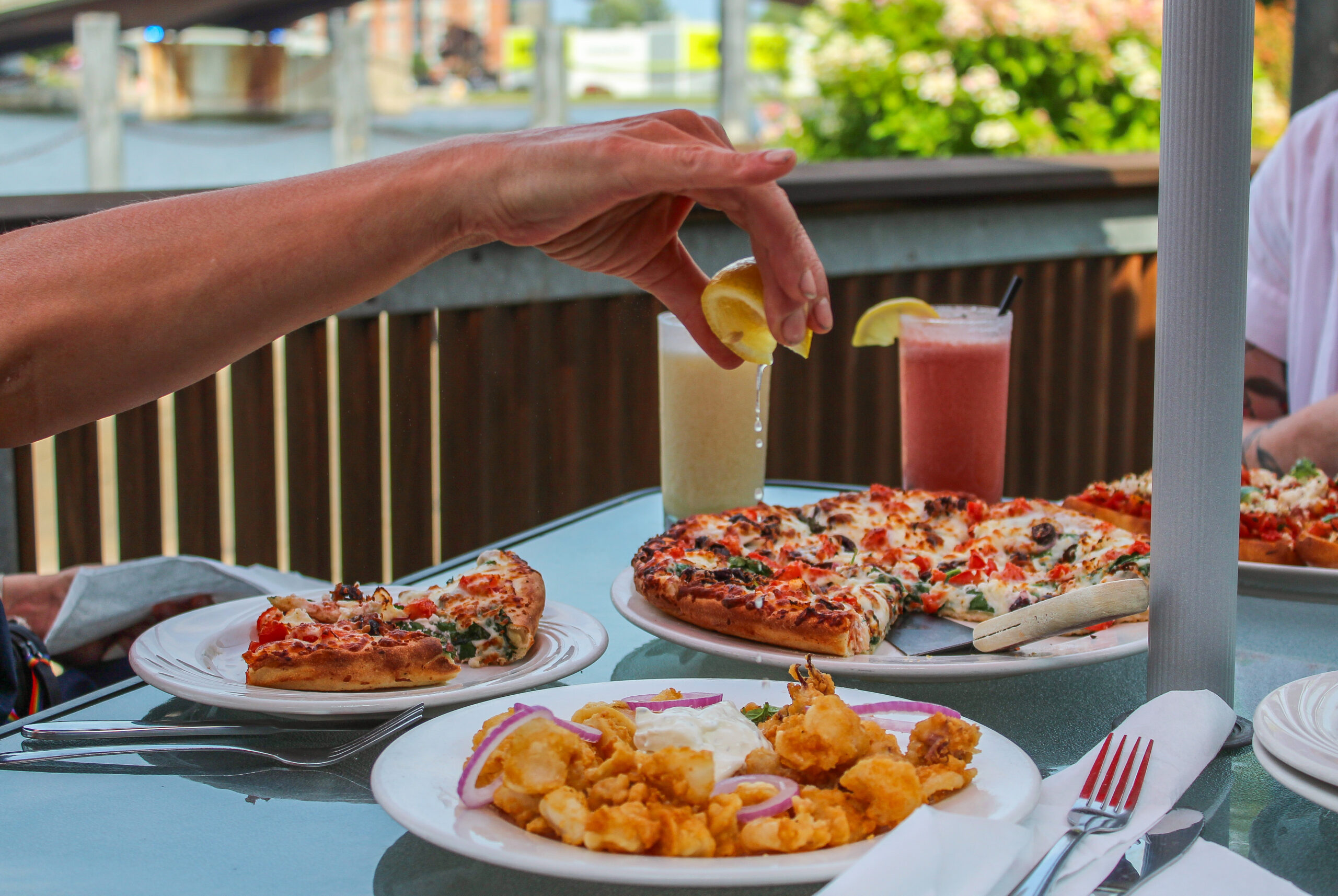 a hand squeezing a lemon over fried calamari on a patio table full of other food