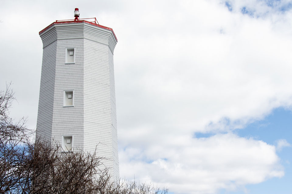 a tall white tower with a red top on a cloudy day.