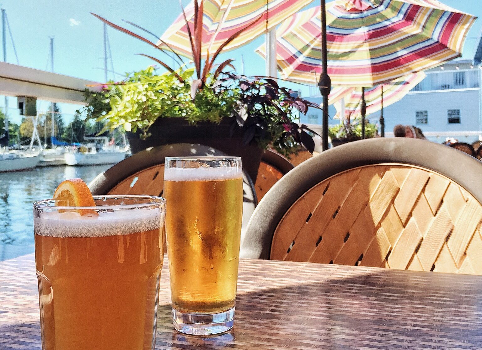 a patio table with umbrella and beer pints, with a marina full of boats in the background
