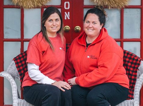 two women sitting on a bench in front of a red door.