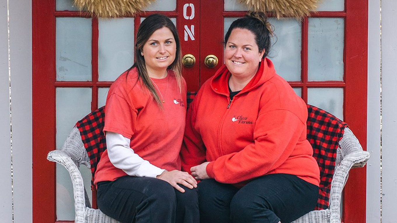 two women sitting on a bench in front of a red door.