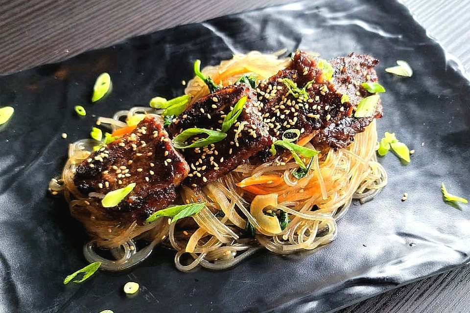 a black plate topped with noodles and meat.