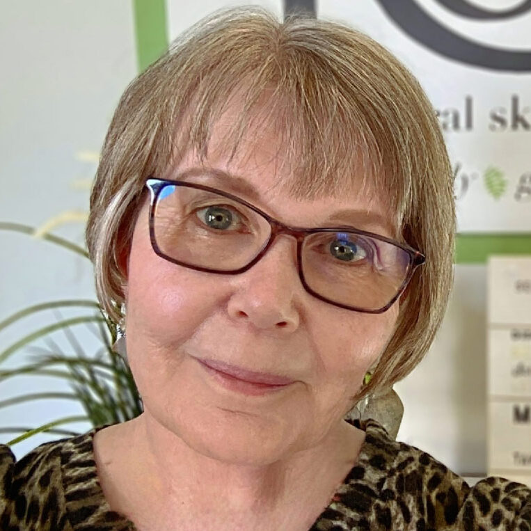 a woman wearing glasses standing in front of a sign.