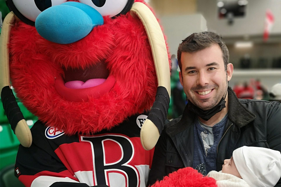 a man holding a baby in front of a mascot.