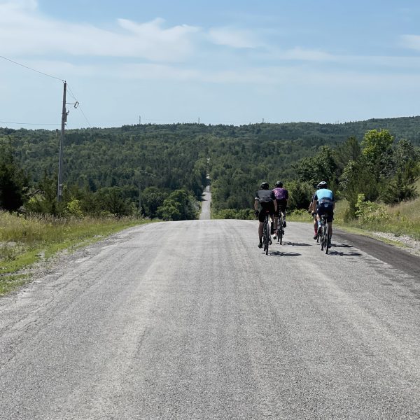 three cyclists cresting over a hill on a gravel backroad