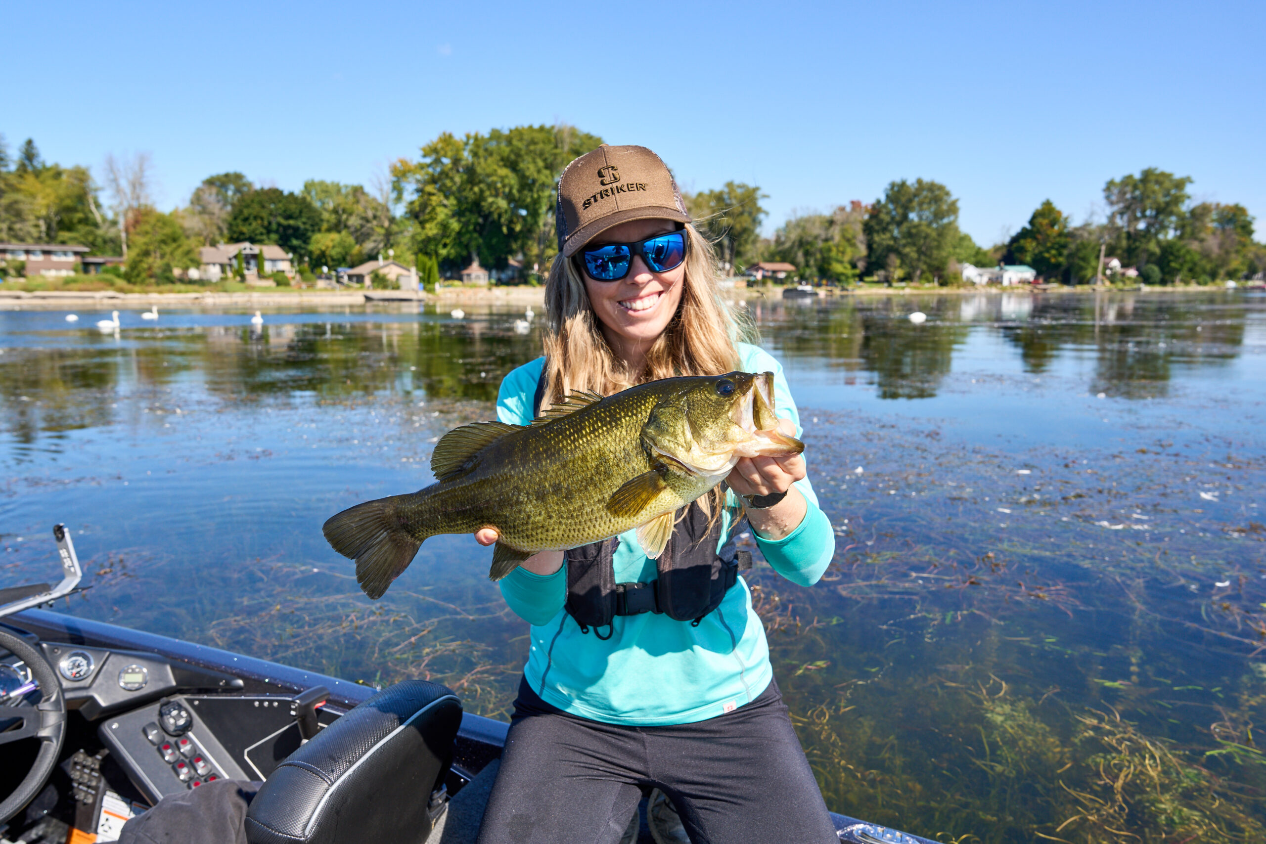 ashley (white woman with long blonde hair) kneeling on a fishing boat showing off the bass she caught