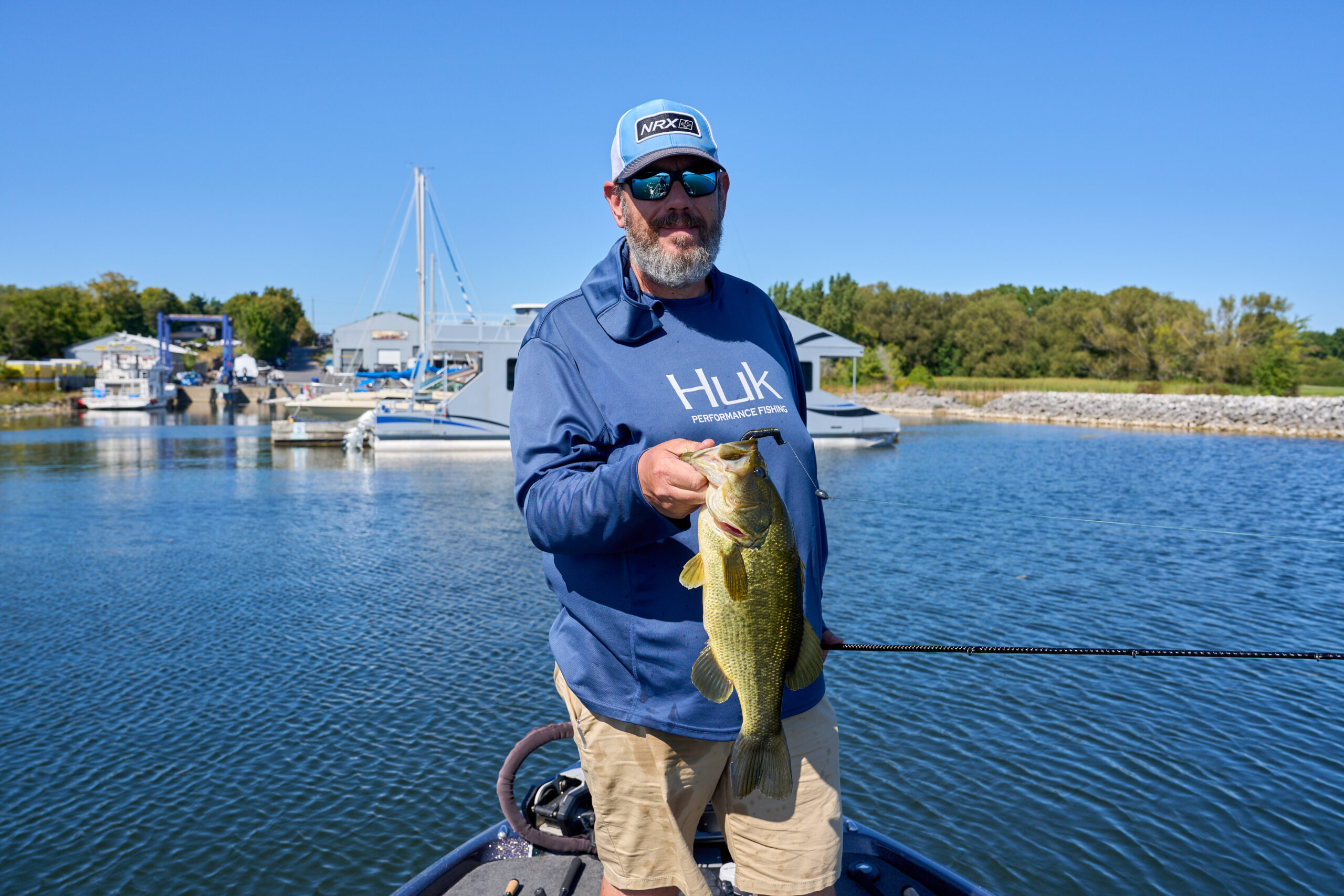 a man standing on a fishing boat with the water in the background holding up a bass fish that he caught