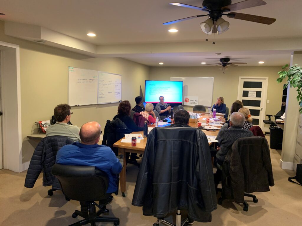 a group of volunteers sitting around a board room table watching a training video