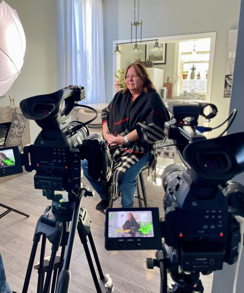 a woman sitting in a chair being interviewed with cameras set up in the foreground