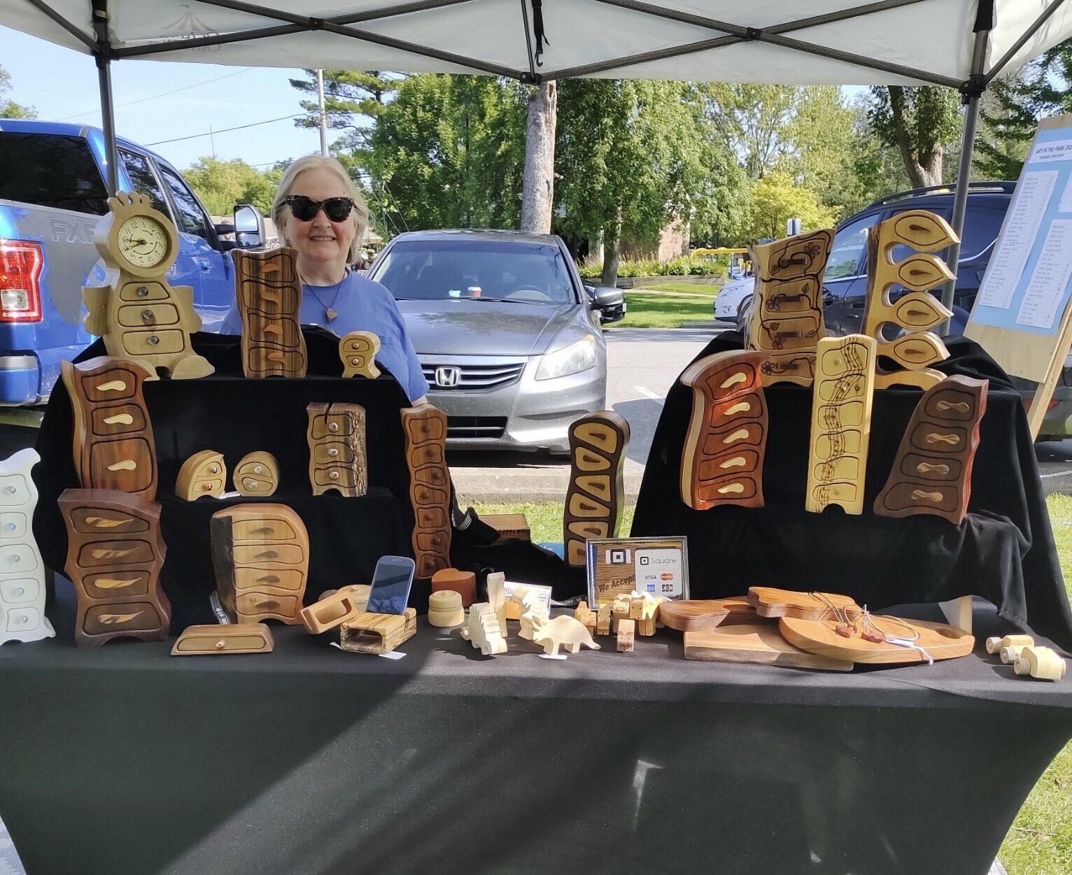 an artist standing behind a table in a display tent showing off woodworking pieces