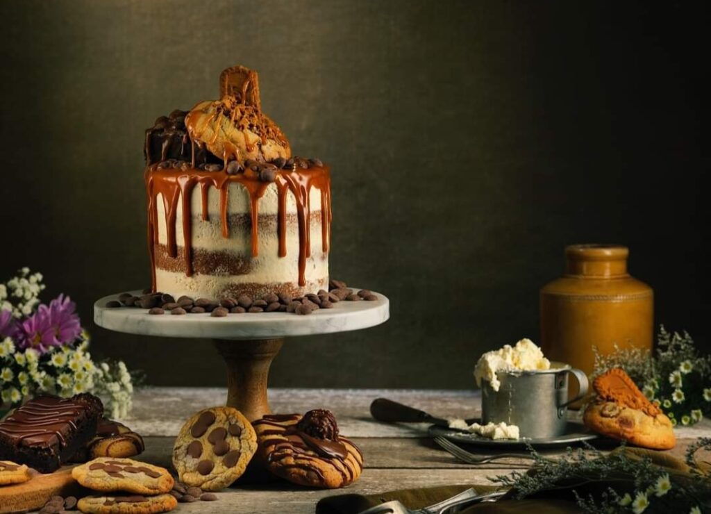 a custom, professionally made cake on a tier with other items like cookies and coffee mugs around it