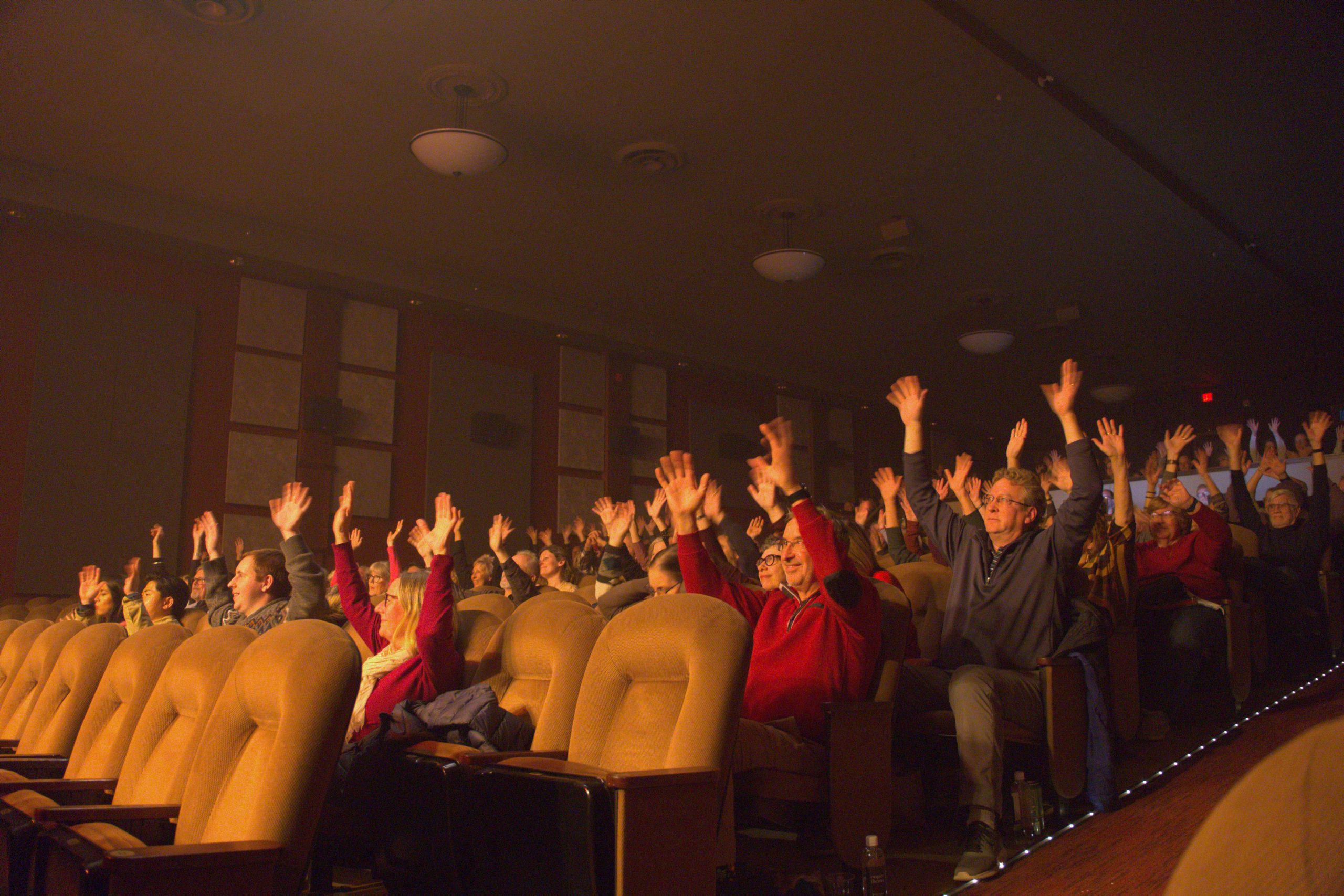 an audience in a theatre all cheering with their hands up