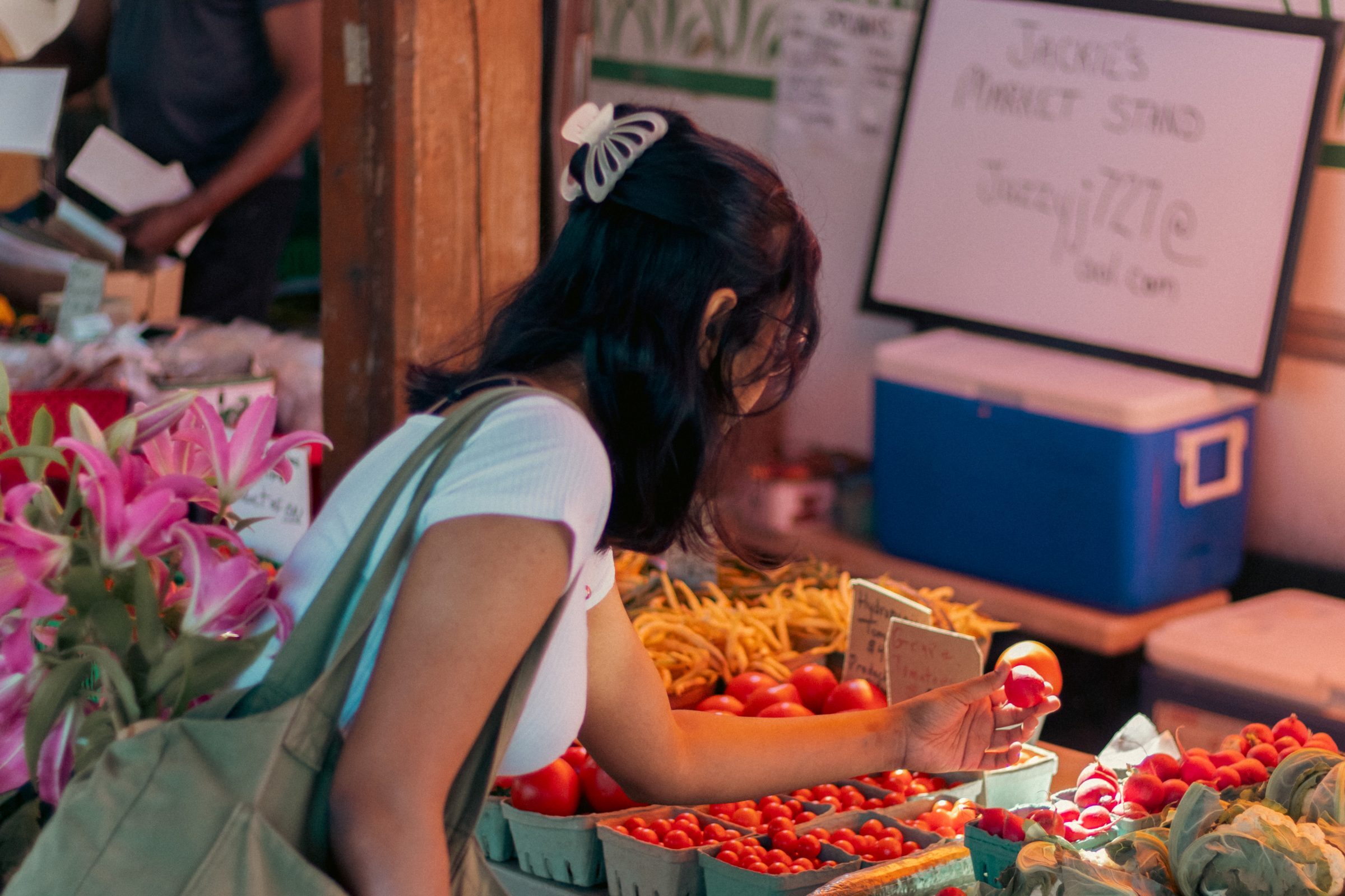 Image of a person holding a tomato at a farmers' market table of vegetables