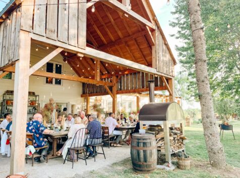 a group of people dining at long tables at oliver farms during an outdoor supper club event