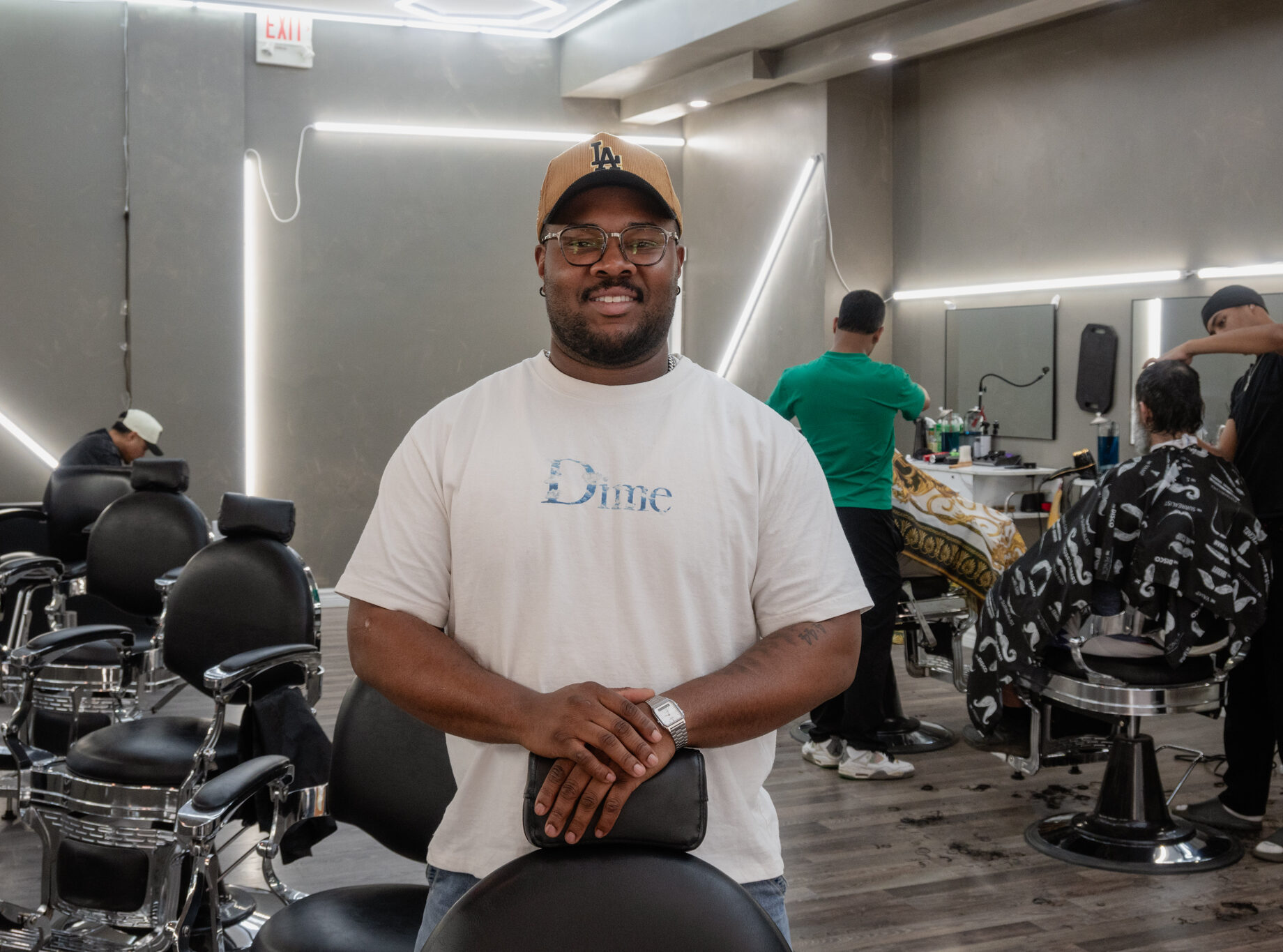 Kam, owner of revive studios, poses for a photo leaning on one of the barber chairs with two employees working in the background